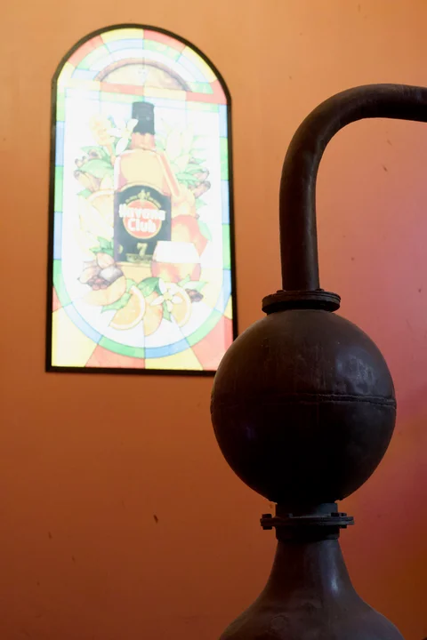 A round metal vessel and curved pipe in front of a Havana Club stained-glass window