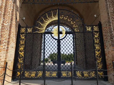 A black iron gate with gold sunburst decoration beneath a brick arch.