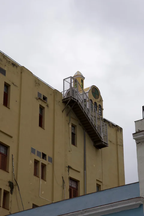 An exterior metal staircase climbing a yellow Havana building towards an ornate rooftop