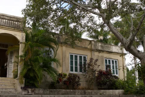 The pale facade and arched porch of Finca Vigía behind garden trees