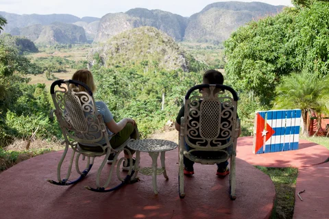 Lena and me in rocking chairs overlooking the valley, beside a wooden panel painted as the Cuban flag