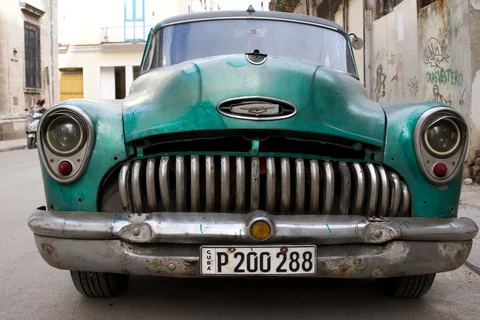 A turquoise vintage car seen head-on in a narrow Havana street