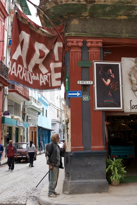 An older man beside a red art banner at a workshop entrance on O’Reilly Street