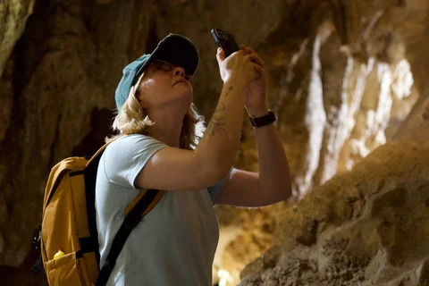 Lena in a green cap with a yellow backpack photographing the cave walls