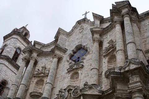 An upward view of a stone church facade with columns, crosses and a stained-glass window